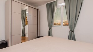 A bedroom with a bed, a window with curtains, and a wardrobe with sliding doors. - Apartman Barbara 4 by Villas Guide (Tribunj)