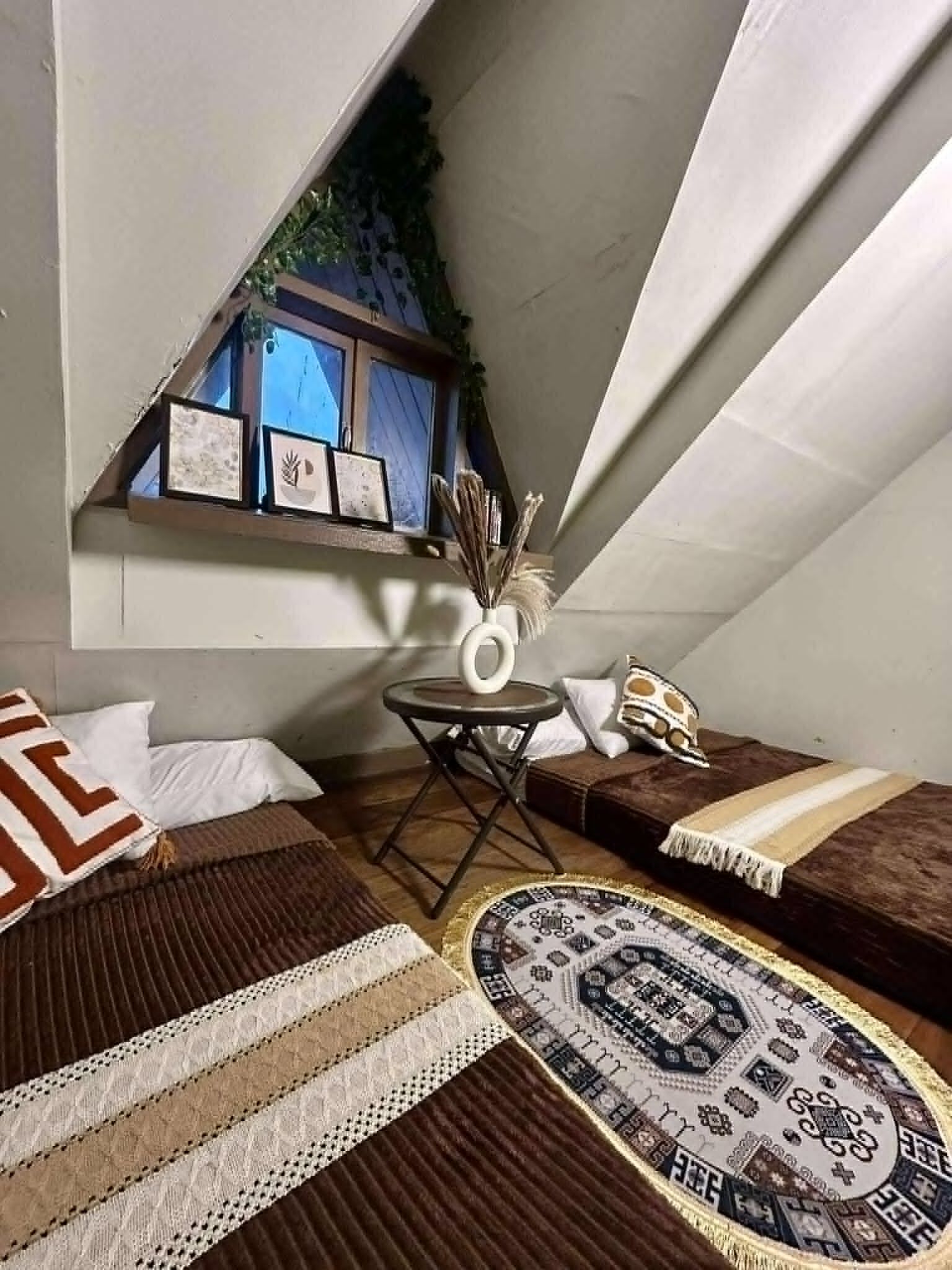 A cozy attic bedroom with a sloped ceiling, a small table with a vase, and a patterned rug.