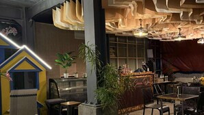 Ein moderner Lounge-Bereich mit einer Couch, Tischen und Stühlen. Eine Bar mit einer Theke und Hockern ist ebenfalls vorhanden.