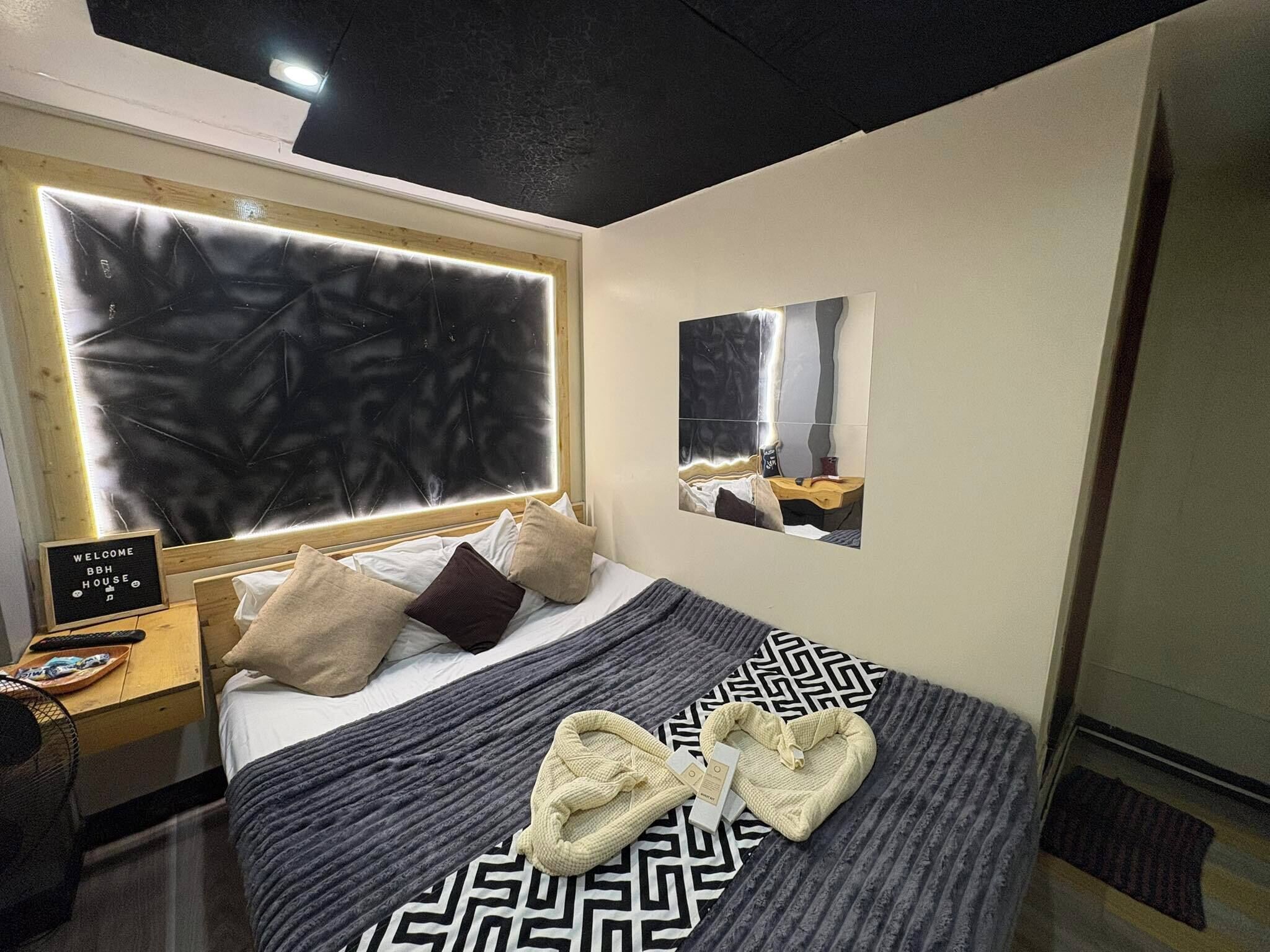 A hotel room with a large bed, a bedside table with a remote control, a welcome sign, and a mirror on the wall.