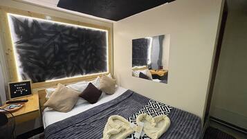 A hotel room with a large bed, a bedside table with a remote control, a welcome sign, and a mirror on the wall.