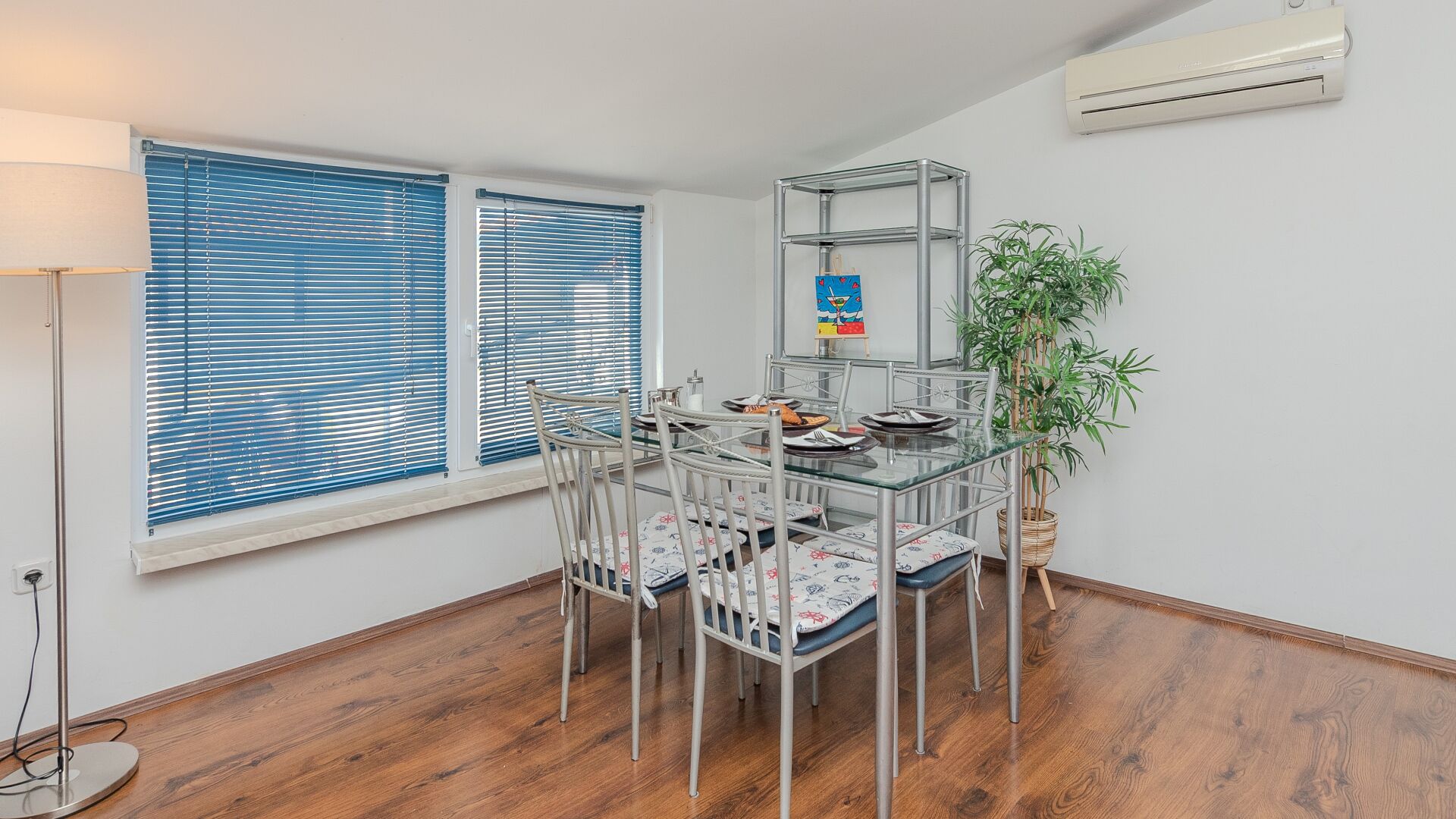 Un coin repas avec une table et des chaises en verre, une étagère en métal et une plante en pot.