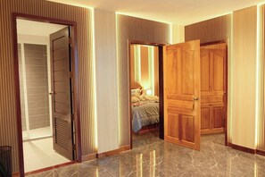Un couloir avec des portes en bois, un lit recouvert d’une courtepointe blanche et une salle de bain équipée d’un porte-serviettes.