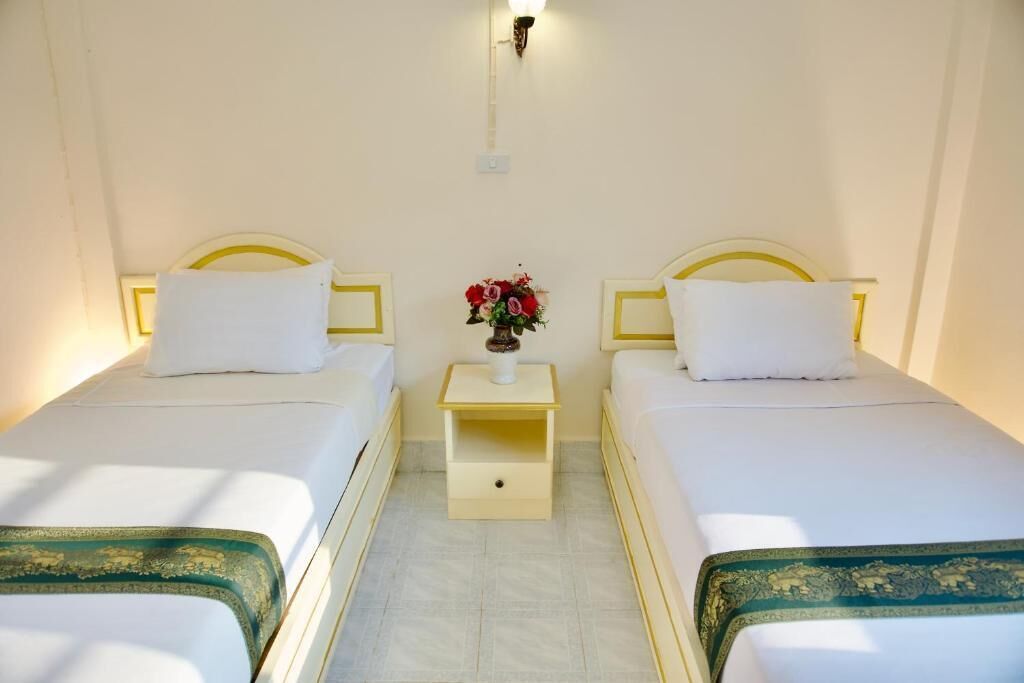 Habitación de hotel con dos camas individuales, una mesita de noche con un florero y una lámpara fijada a la pared.