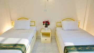 Habitación de hotel con dos camas individuales, una mesita de noche con un florero y una lámpara fijada a la pared.