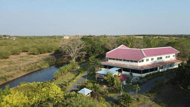 Un grand bâtiment à toit rouge, entouré de verdure et bordé par une rivière.
