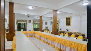 Une salle de conférence avec une longue table, des nappes jaunes et blanches, des chaises en bois et un grand tableau encadré au mur.