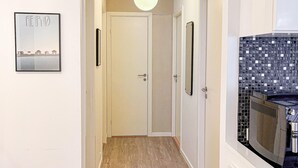 Un couloir étroit avec un plancher en bois, des murs blancs et un luminaire au plafond. Un tableau encadré est accroché au mur et un four à micro-ondes se trouve sur le côté droit.