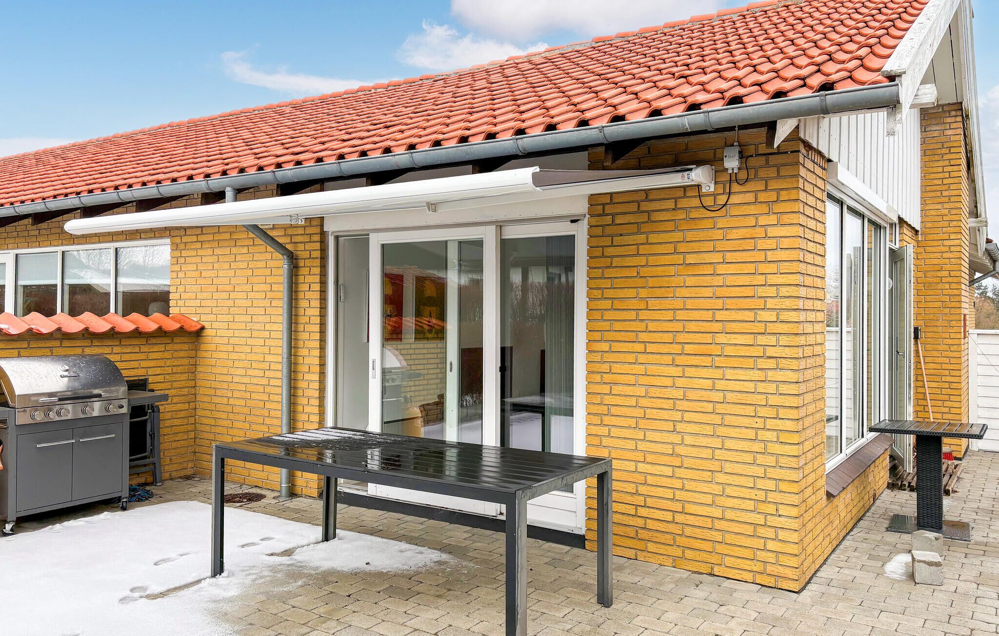A patio with a grill, a table, and a covered area with a red-tiled roof.