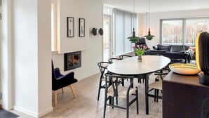 Un salon moderne avec une table de salle à manger ronde, des chaises noires, un canapé noir et une grande fenêtre avec des stores.