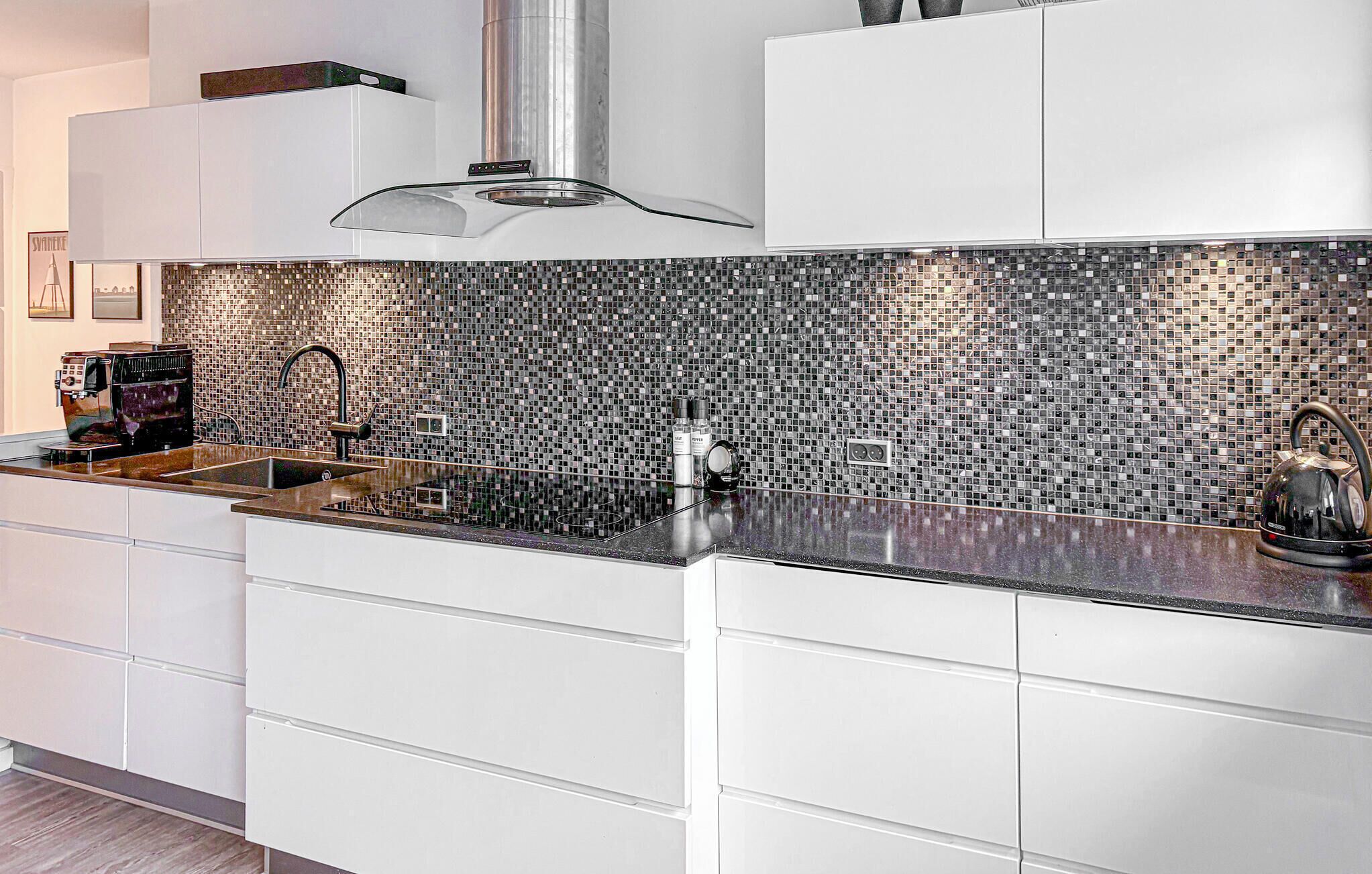 A modern kitchen with white cabinetry, a black tiled backsplash, and stainless steel appliances.