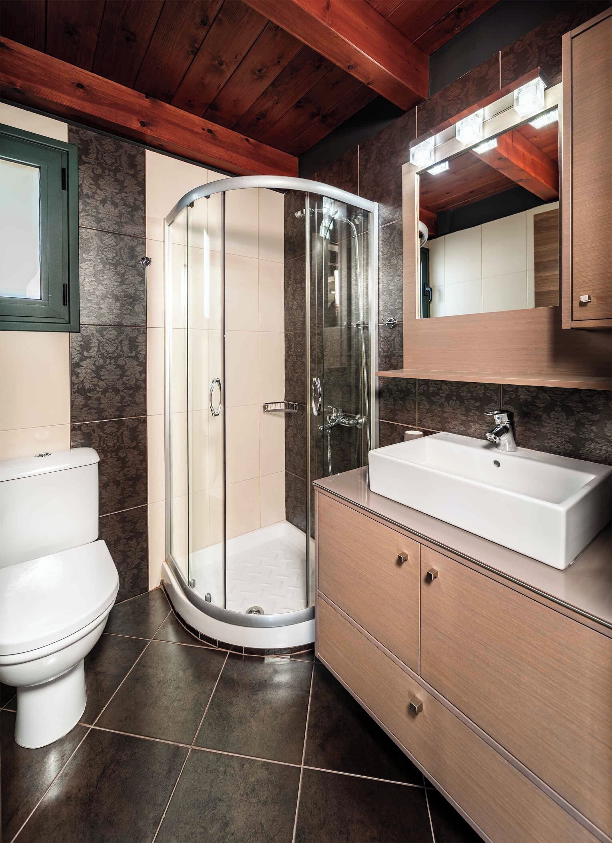 A bathroom with a glass shower enclosure, a white sink, and a wooden vanity.