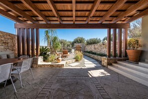 Eine Außenpatio-Terrasse mit einer Holzpergola, Steinmauern, einem Steinweg und Gartenmöbeln.