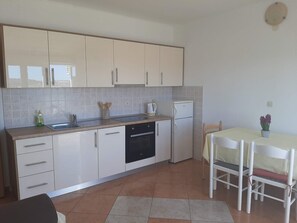 A compact kitchen with white cabinets, a dishwasher, and a small refrigerator. There is a dining table with chairs and a vase of flowers. - Apartments Donadić, Caska, Novalja, Island Pag, Zrće (Caska)