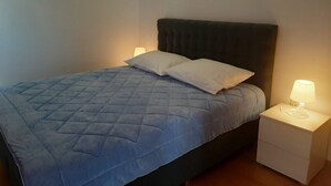 Een slaapkamer met een bed, twee kussens, een nachtkastje met een lamp en een witte muur.