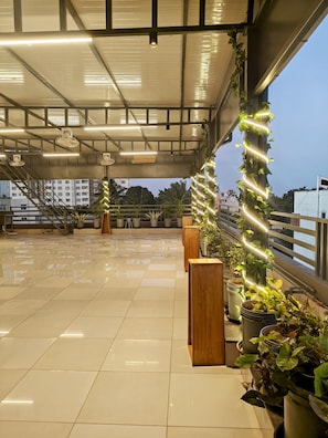 A spacious indoor area with a tiled floor, ceiling lights, and potted plants arranged along the walls. - Fortale Prime | Serviced Apartment (Bengaluru)