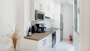 Eine moderne Küche mit weißen Schränken, einer Mikrowelle, einer Kaffeemaschine und einer Weinflasche.
