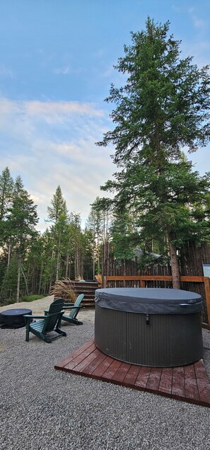 A hot tub surrounded by Adirondack chairs on a gravel deck, with a wooden fence and trees in the background. - NEW 9-cabin micro-resort, Full Buy Out-private, 2 hot tubs, 2 saunas,sleeps 24 (Whitefish)