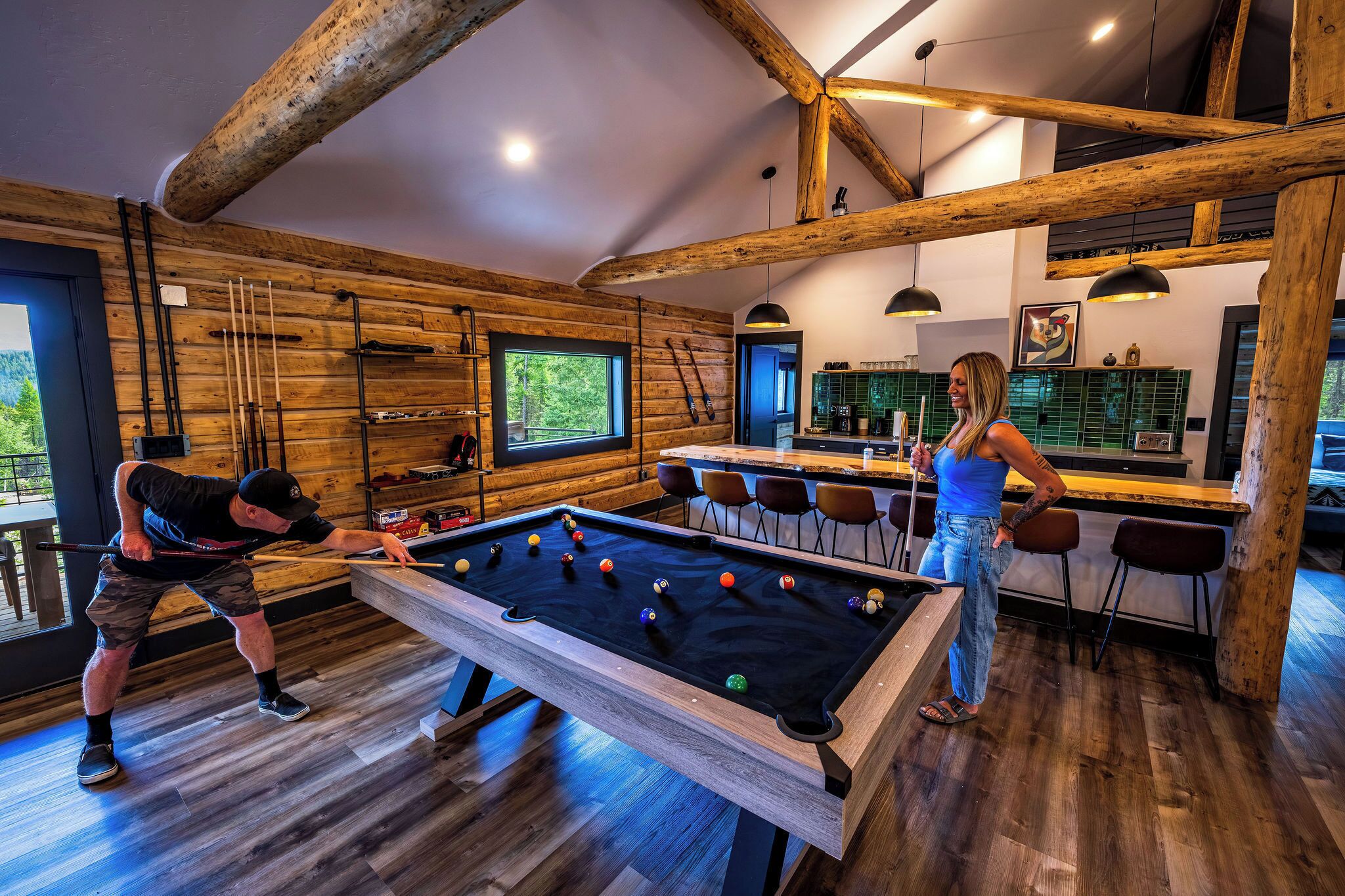 Un intérieur en bois avec une table de billard, un coin bar et une lumière naturelle provenant des fenêtres.