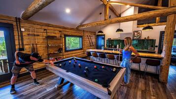 Un intérieur en bois avec une table de billard, un coin bar et une lumière naturelle provenant des fenêtres.
