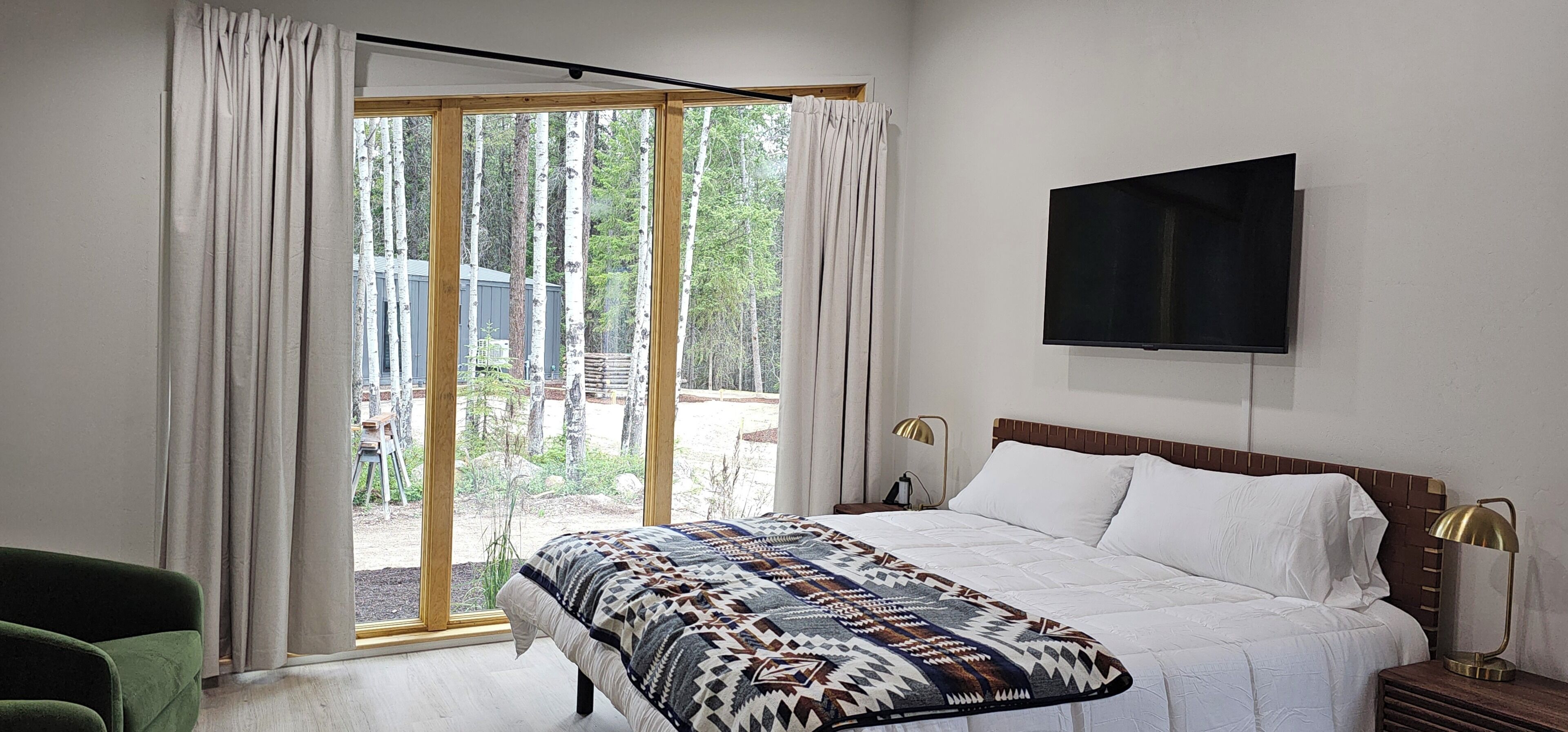 A bedroom with a bed, a TV mounted on the wall, and a view of trees through the window.