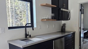 A modern kitchen with a built-in sink, black cabinets, a microwave, and a window with a view of trees. - NEW 9-cabin micro-resort, Full Buy Out-private, 2 hot tubs, 2 saunas,sleeps 24 (Whitefish)