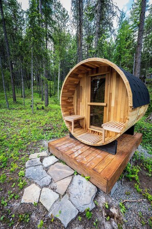 A wooden cylindrical structure with a bench and a table, surrounded by a forest.