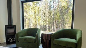 A bedroom with a large window, two green armchairs, a small wooden table, and a black heater. - NEW 9-cabin micro-resort, Full Buy Out-private, 2 hot tubs, 2 saunas,sleeps 24 (Whitefish)