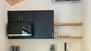 A modern kitchen with black cabinets, a stainless steel refrigerator, a microwave, and a coffee maker. There is a wooden shelf above the sink and a window above the microwave. - NEW 9-cabin micro-resort, Full Buy Out-private, 2 hot tubs, 2 saunas,sleeps 24 (Whitefish)