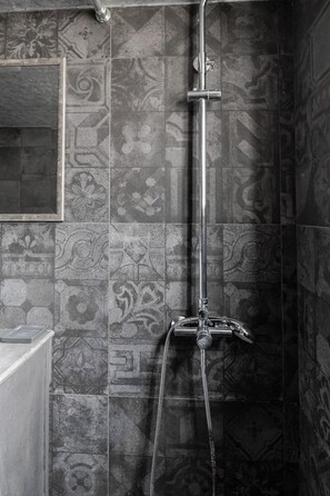 Une salle de bain avec des carreaux décorés, une douche équipée d’un pommeau de douche amovible et un miroir au mur.