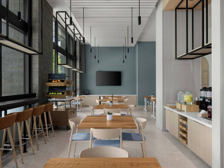 A modern cafe with wooden tables and chairs, a kitchen area, and a large window.