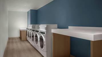 A laundry room with a row of front-loading washers and dryers, wooden cabinets, and a blue accent wall.