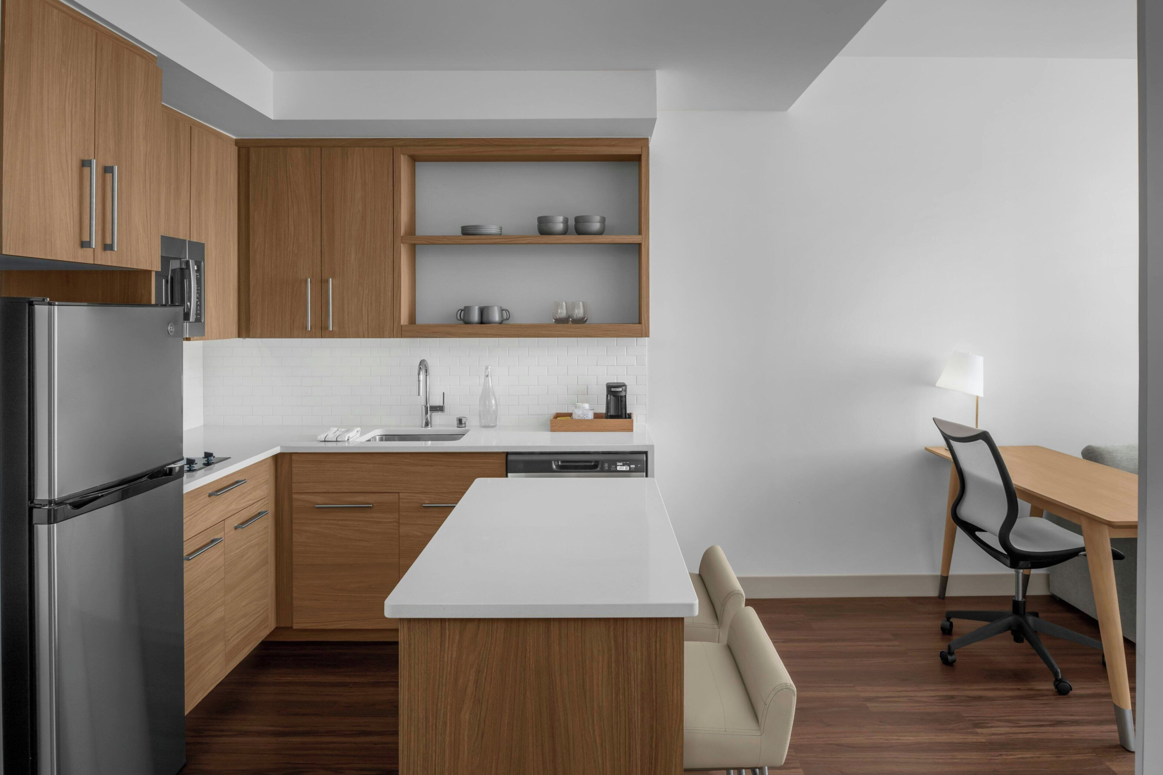 Cocina moderna con armarios de madera, refrigerador de acero inoxidable, encimera blanca y lavavajillas integrado.