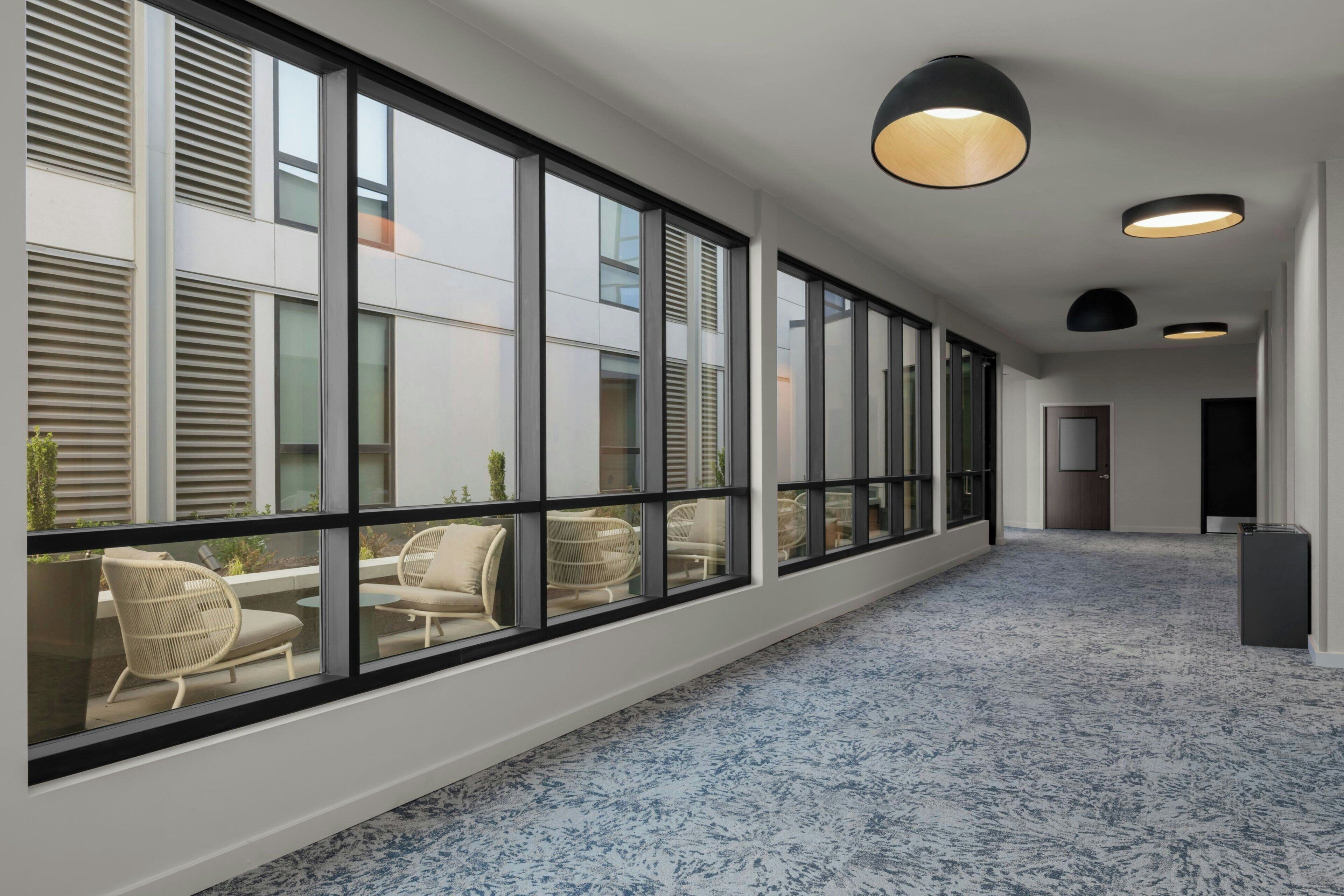 A corridor with large windows, a patterned carpet, and modern lighting fixtures.