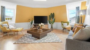 Un salon moderne doté d’un grand téléviseur à écran plat, d’une table basse et de deux fauteuils.