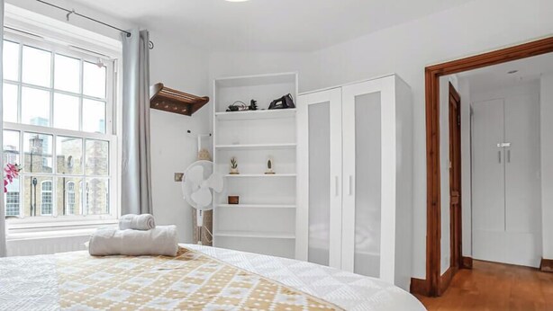 Ein Schlafzimmer mit einem großen Bett, einem weißen Kleiderschrank, einer weißen Regalwand und Holzboden.