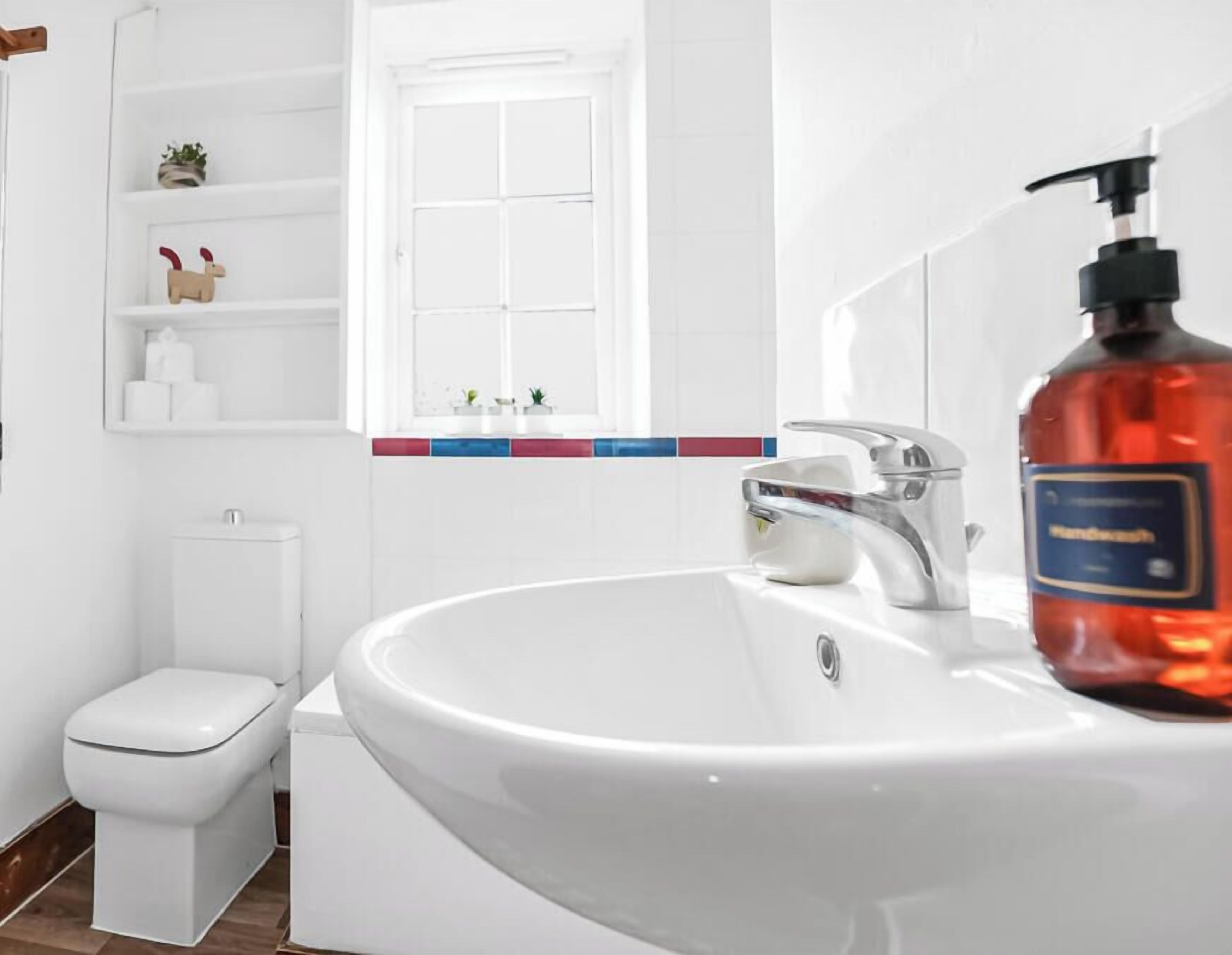 Een badkamer met een wit wastafelmeubel, een toilet en een plank met toiletartikelen.