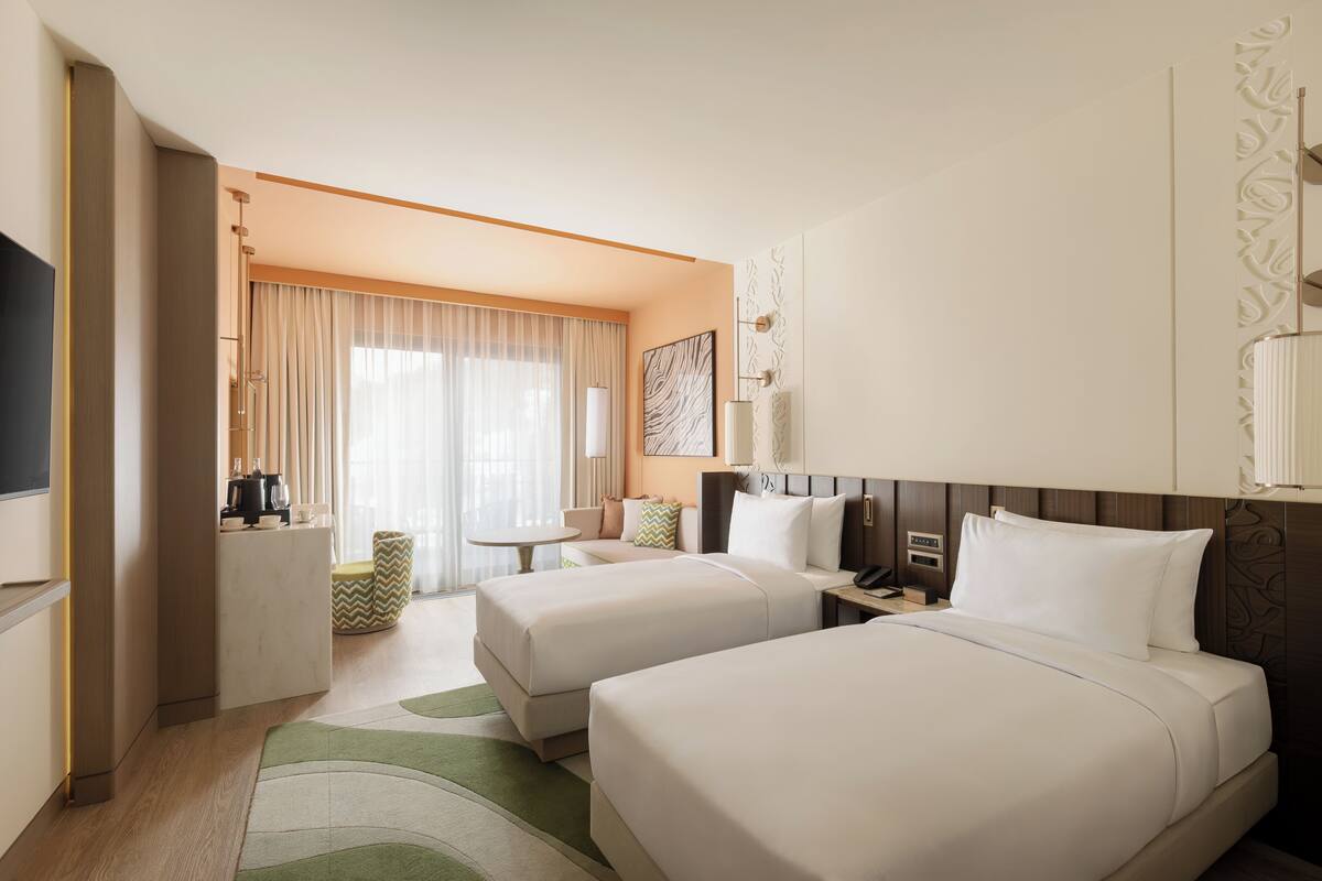 A hotel room with two beds, a desk, a chair, a TV, and a bathroom.