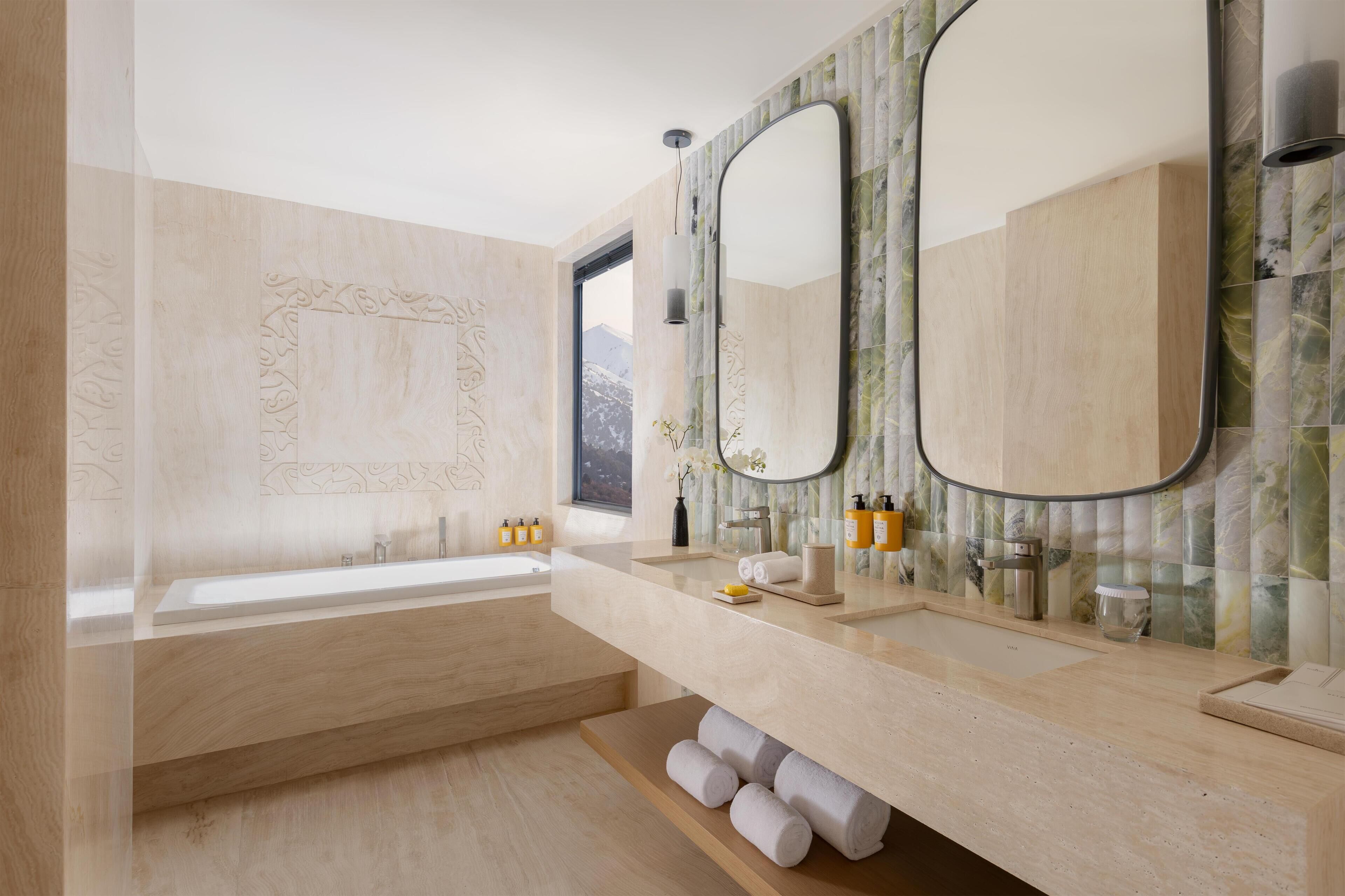 A modern bathroom with a bathtub, two sinks, and a large mirror.