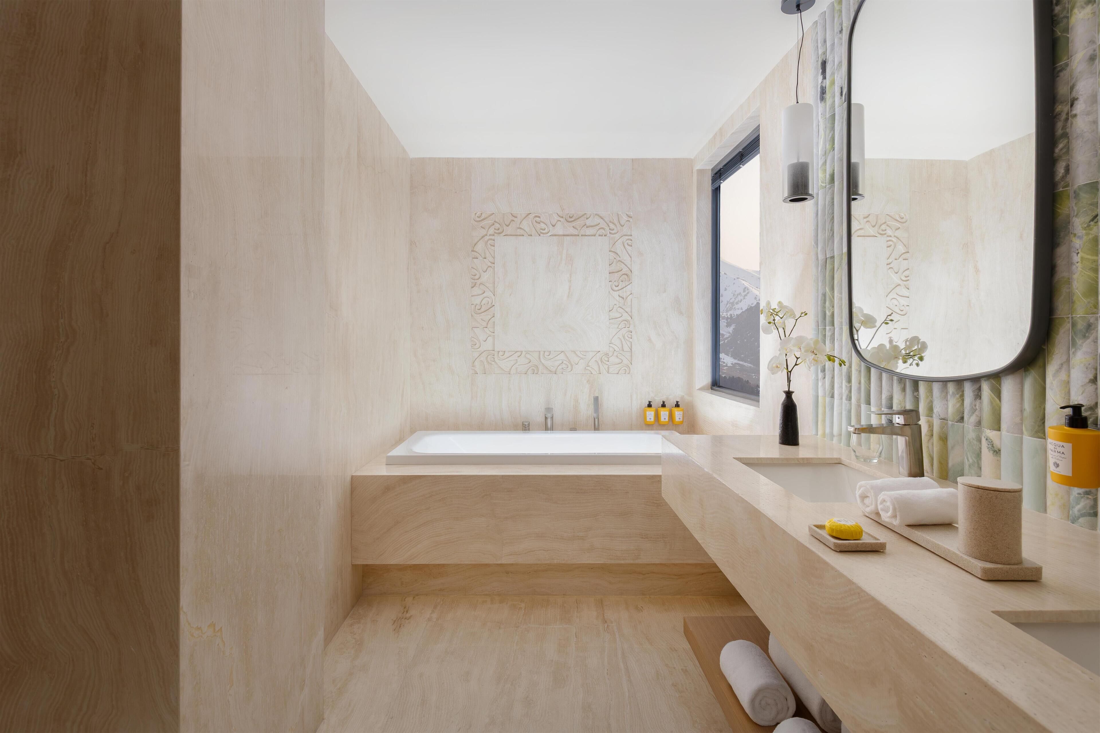 Un baño moderno con una bañera grande, un tocador con espejo y un ventanal con vistas.