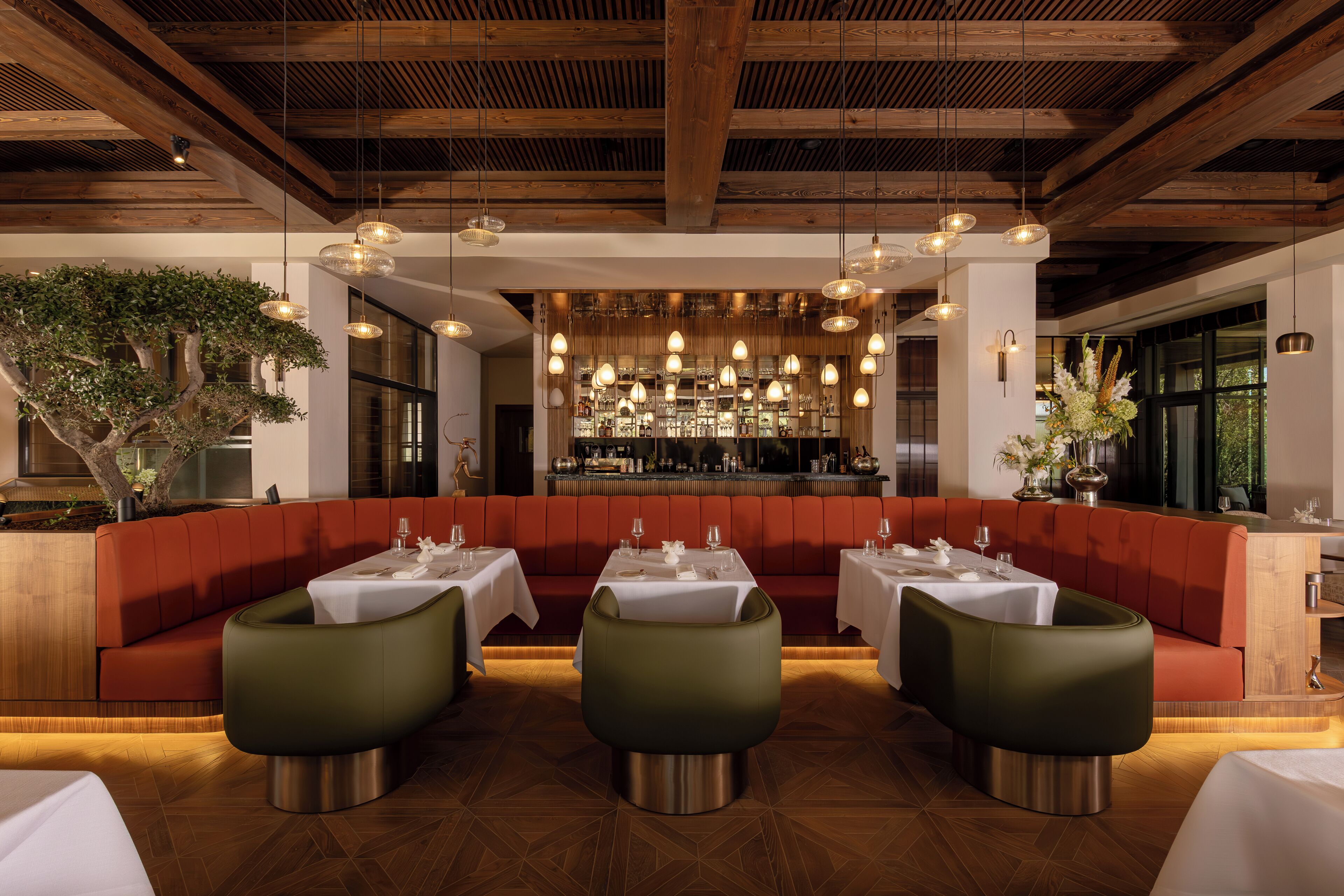 A restaurant interior with wooden beams, green upholstered seating, and a bar area with glassware.