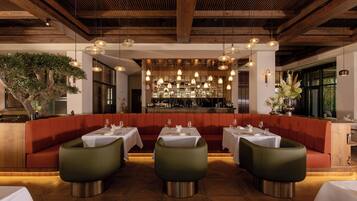 A restaurant interior with wooden beams, green upholstered seating, and a bar area with glassware.