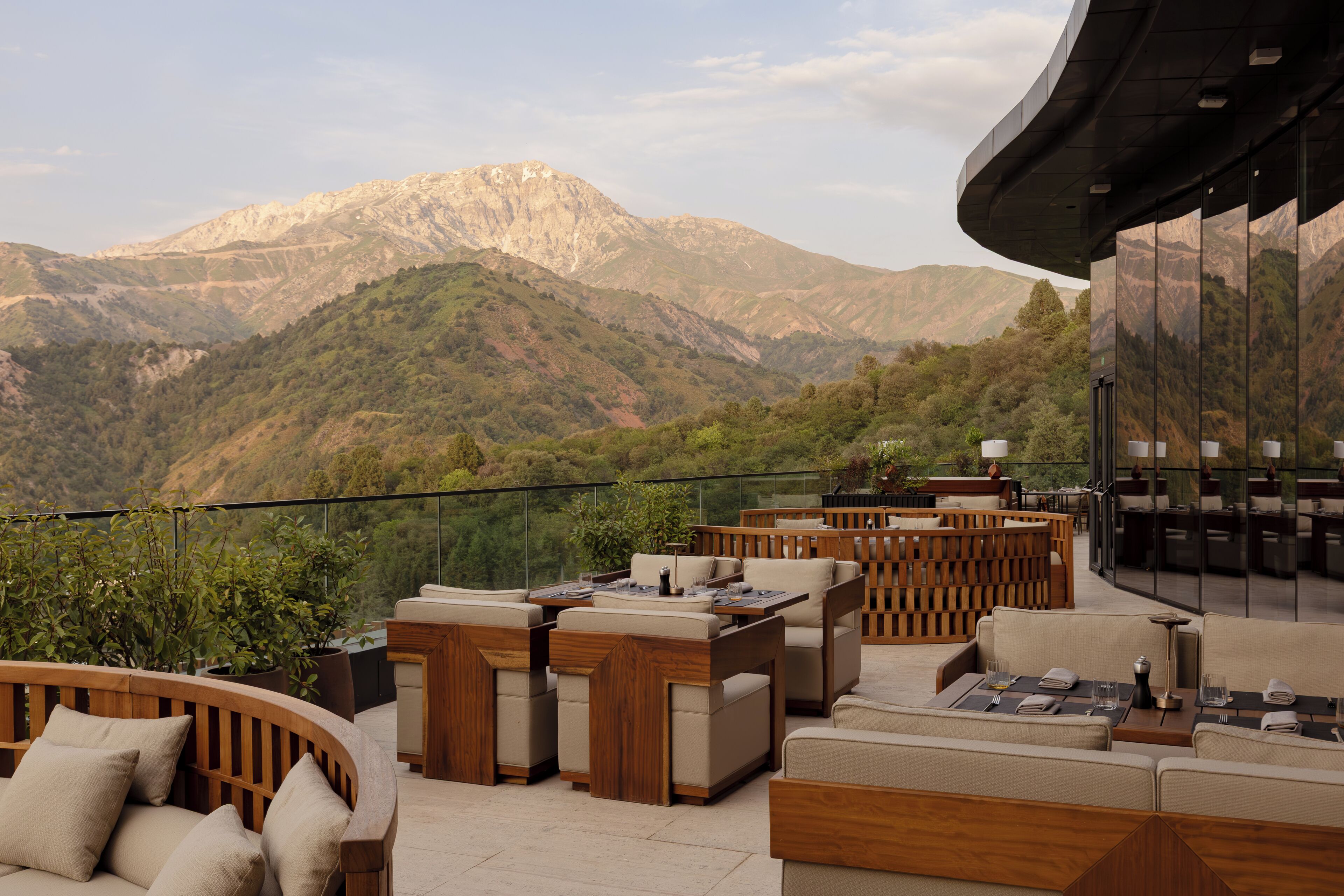 Una terraza con mobiliario exterior, barandilla de vidrio y montañas al fondo.