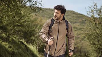A person hiking with a backpack and walking stick in a forested area.