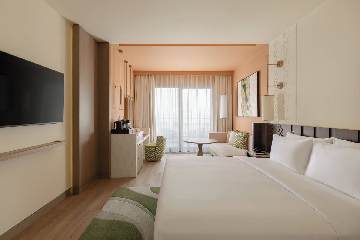 Habitación de hotel con una cama grande, un escritorio, una silla, un televisor y una ventana con cortinas.