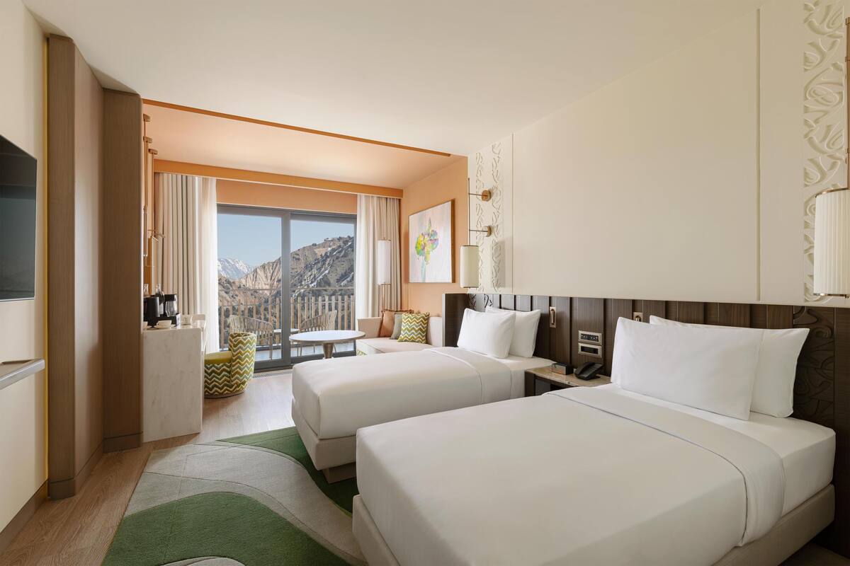 A hotel room with two beds, a dining area, a kitchen, and a large window with a mountain view.