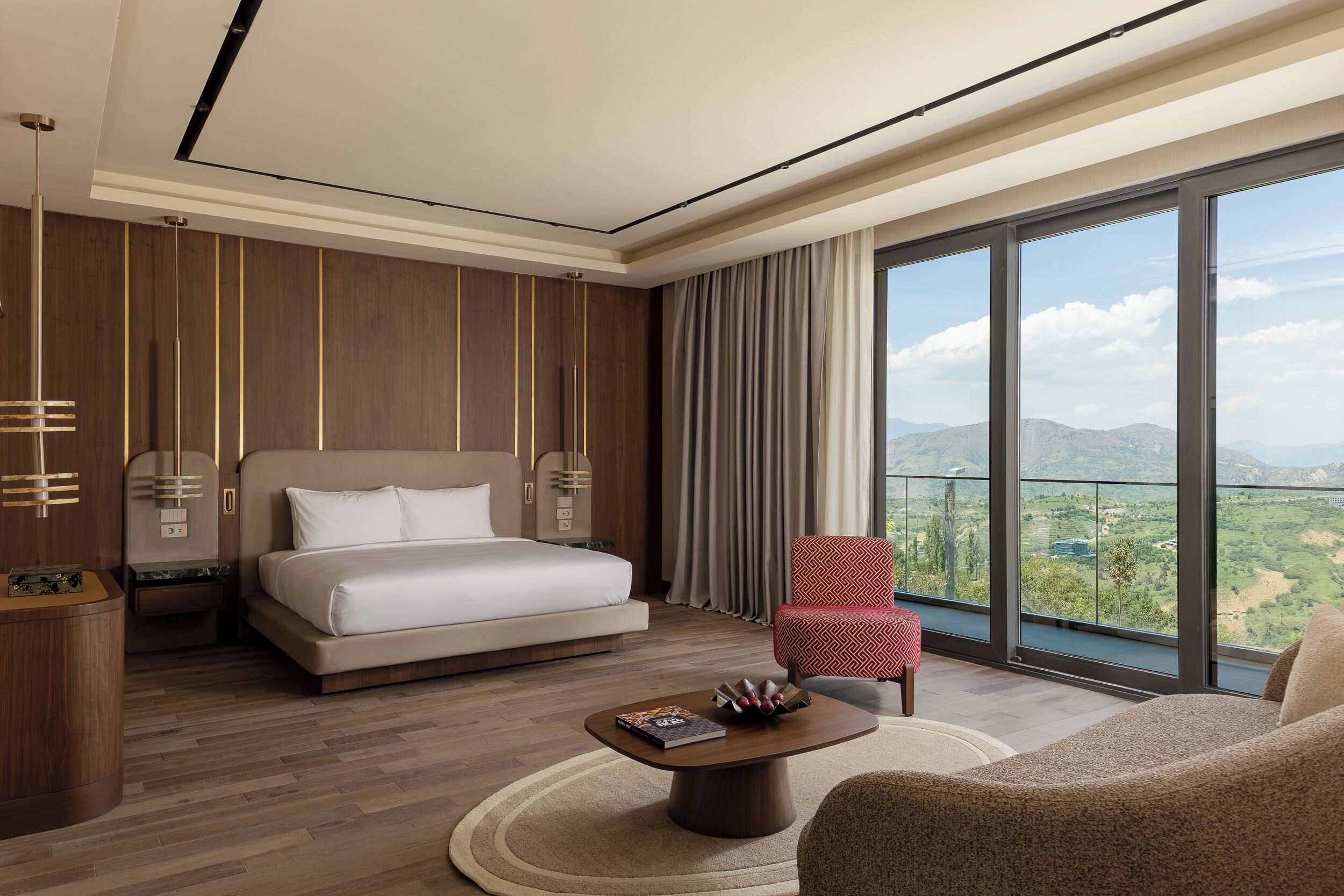 Une chambre d’hôtel moderne dotée d’un grand lit, d’un coin salon avec une table basse et d’une vue sur la campagne.