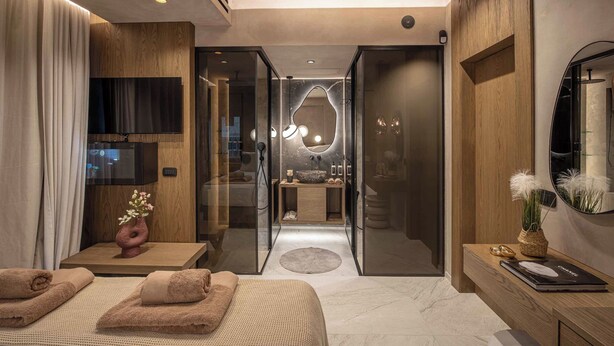 Ein modernes Schlafzimmer mit Bett, Fernseher und einem Badezimmer inklusive Spiegel und Dusche.