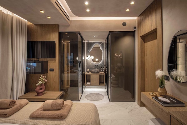 A modern bedroom with a bed, a TV, a bathroom with a mirror, and a shower.