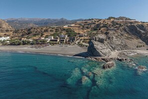 A coastal town with buildings on a hillside, a rocky outcrop, and clear blue waters.